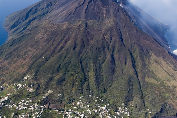 Vista aerea di Stromboli, il vulcano attivo che si erge bruscamente dal mare con fumi che fuoriescono dal cratere.