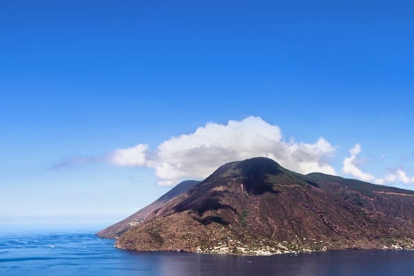 L'isola di Stromboli vista dall'acqua, il suo picco vulcanico che svetta sopra il calmo mare blu.